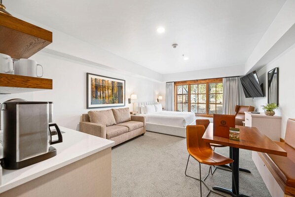 A hotel room with a bed, a sofa, a dining table, a coffee maker, and a TV. - Moonlit Oak | Includes Two 1-Day Lift Tickets (Tamarack)