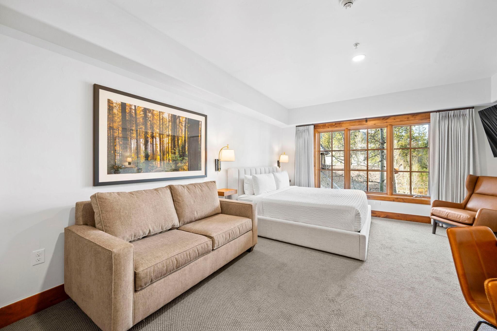 A hotel room with a large bed, a sofa, a desk, and a window with curtains.