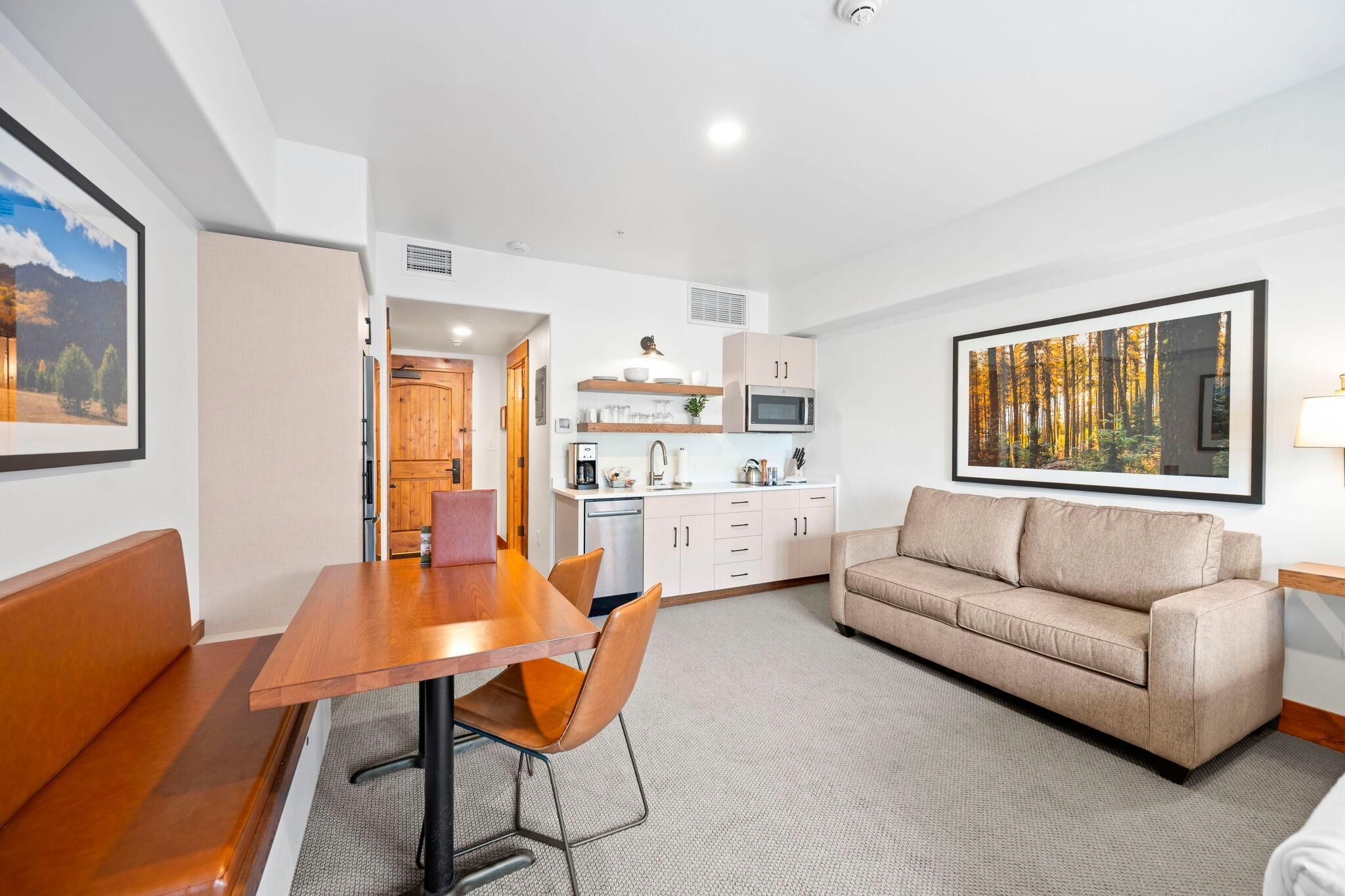 A modern living room with a wooden dining table, beige sofa, and a kitchen in the background.