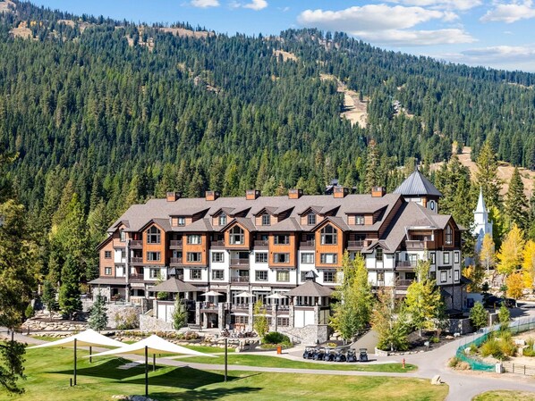 A multi-story hotel with a stone facade, multiple balconies, and a ski resort in the background.