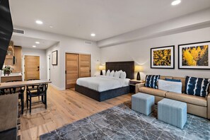 Quarto de hotel moderno com cama, sofá, escrivaninha e espaço para refeições.
