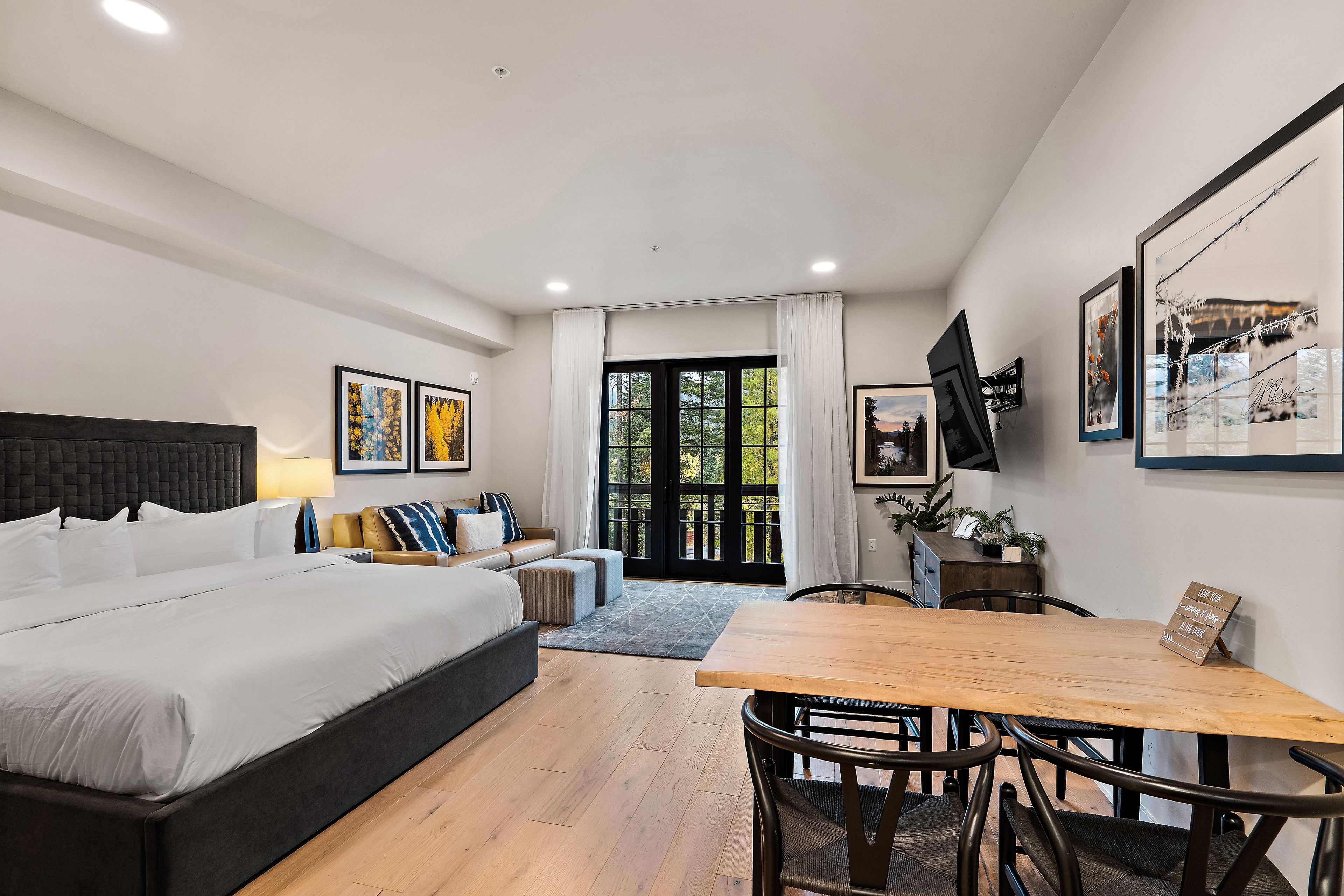 A modern hotel room with a large bed, a dining table, and a TV mounted on the wall.