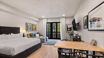 A modern hotel room with a large bed, a dining table, and a TV mounted on the wall.