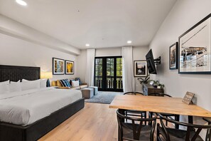 A modern hotel room with a large bed, a dining table, and a TV mounted on the wall. - Polished Condo|Centrally Located with Village Views (Tamarack)