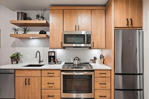 A modern kitchen with wooden cabinets, stainless steel appliances including a microwave and refrigerator, a built-in oven, and a coffee maker.