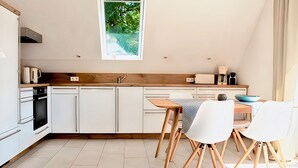 Une cuisine moderne avec des meubles blancs, un plan de travail en bois, un four encastré et un coin repas comprenant une table et des chaises.