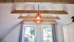 Une pièce avec des poutres apparentes, un luminaire suspendu et de grandes fenêtres dotées de rideaux.