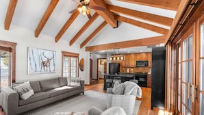 A spacious living area with a large sofa, a smaller chair, and a fireplace. A kitchen with wooden cabinets and a black refrigerator is visible in the background. - Four Reasons | Exclusive Tamarack Perks (Tamarack)