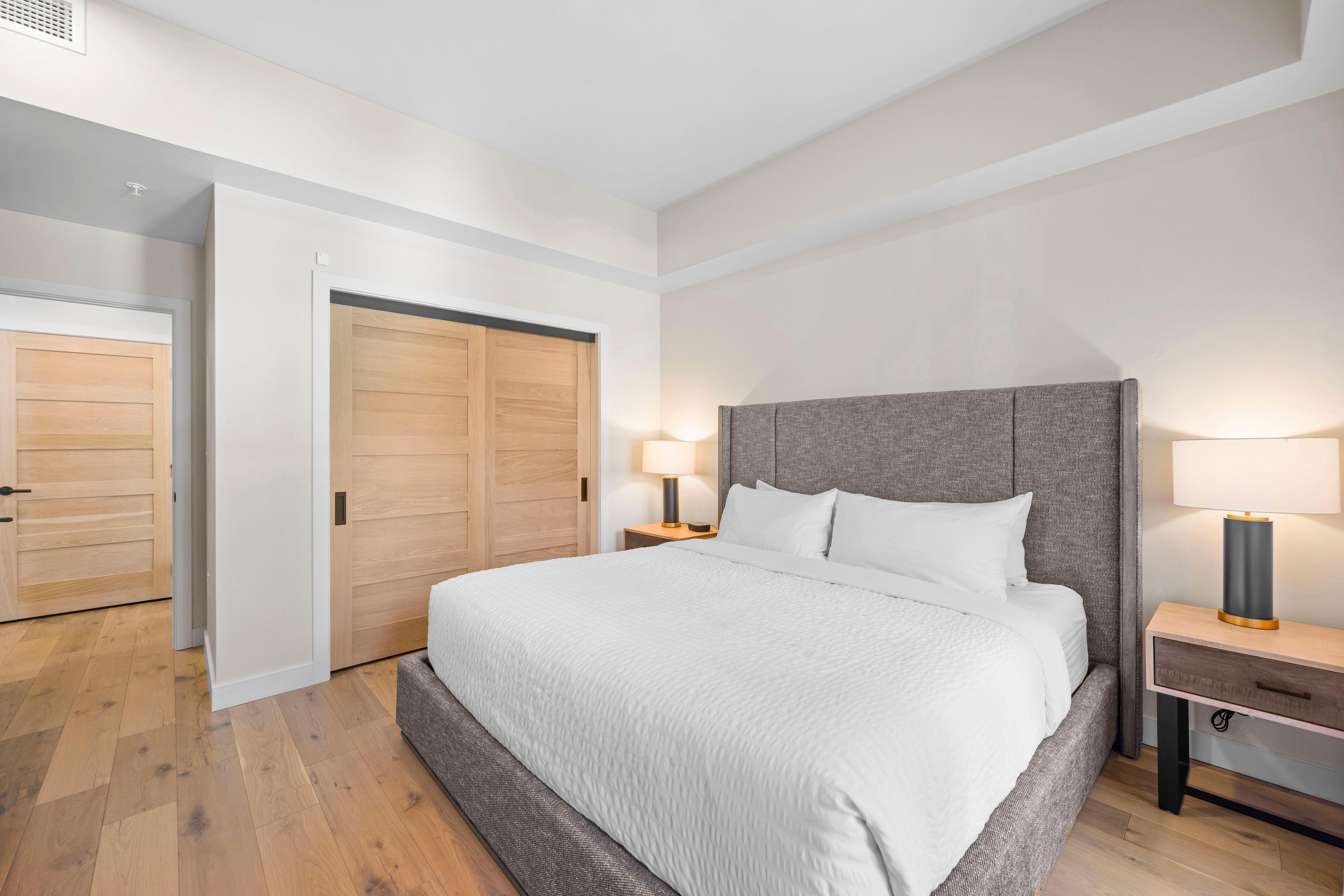 A modern bedroom with a large bed, wooden wardrobe, and bedside lamps.