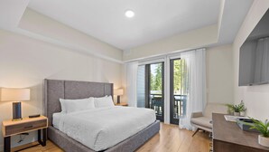 Un dormitorio moderno con una cama grande, mesitas de noche, un escritorio y vistas al exterior.