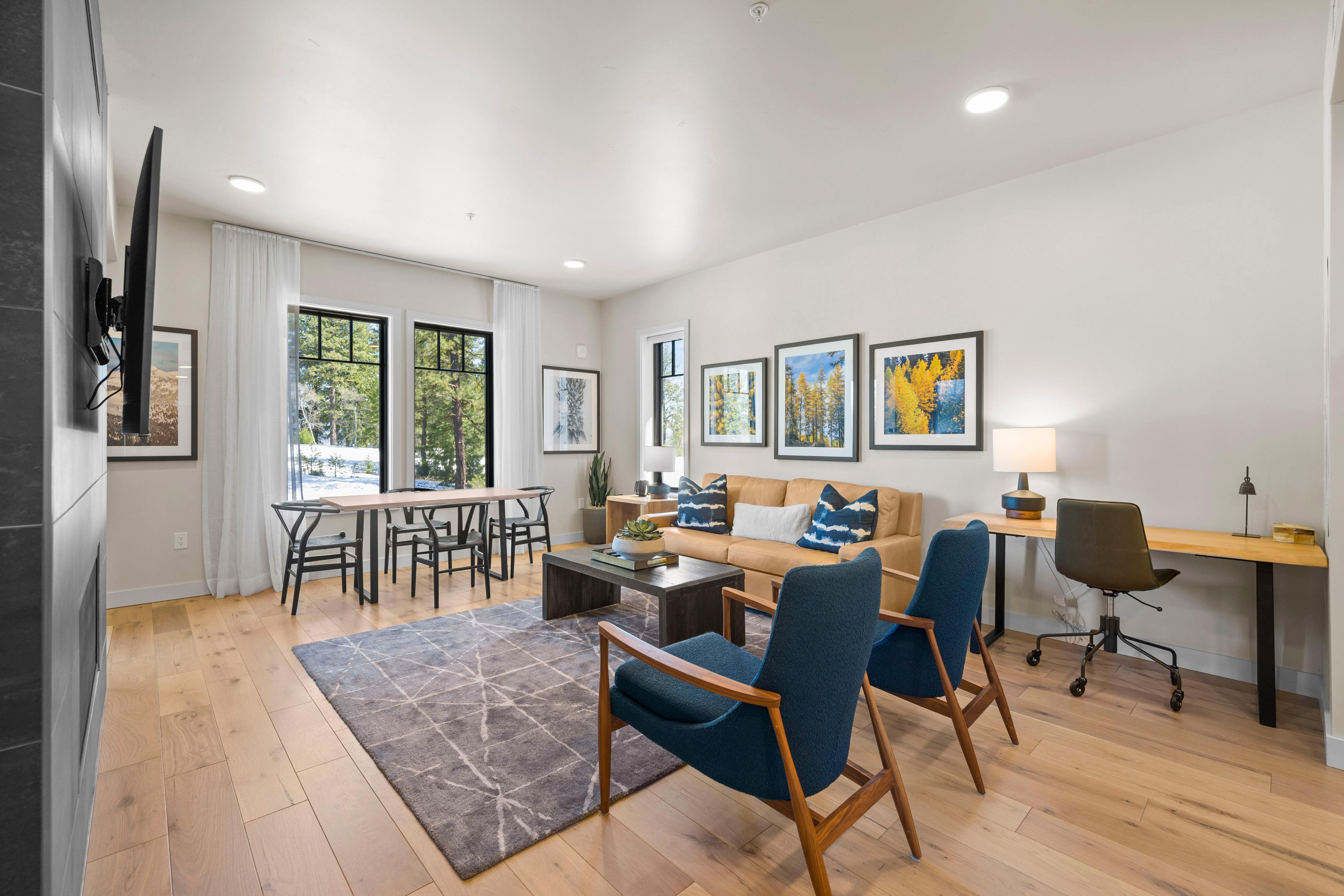 A modern living room with a sofa, chairs, a dining table, and artwork on the walls.