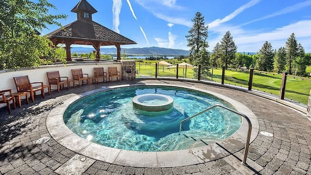 Un bain à remous entouré de carreaux de pierre, de chaises en bois et d’un belvédère offrant une vue sur un terrain de golf.