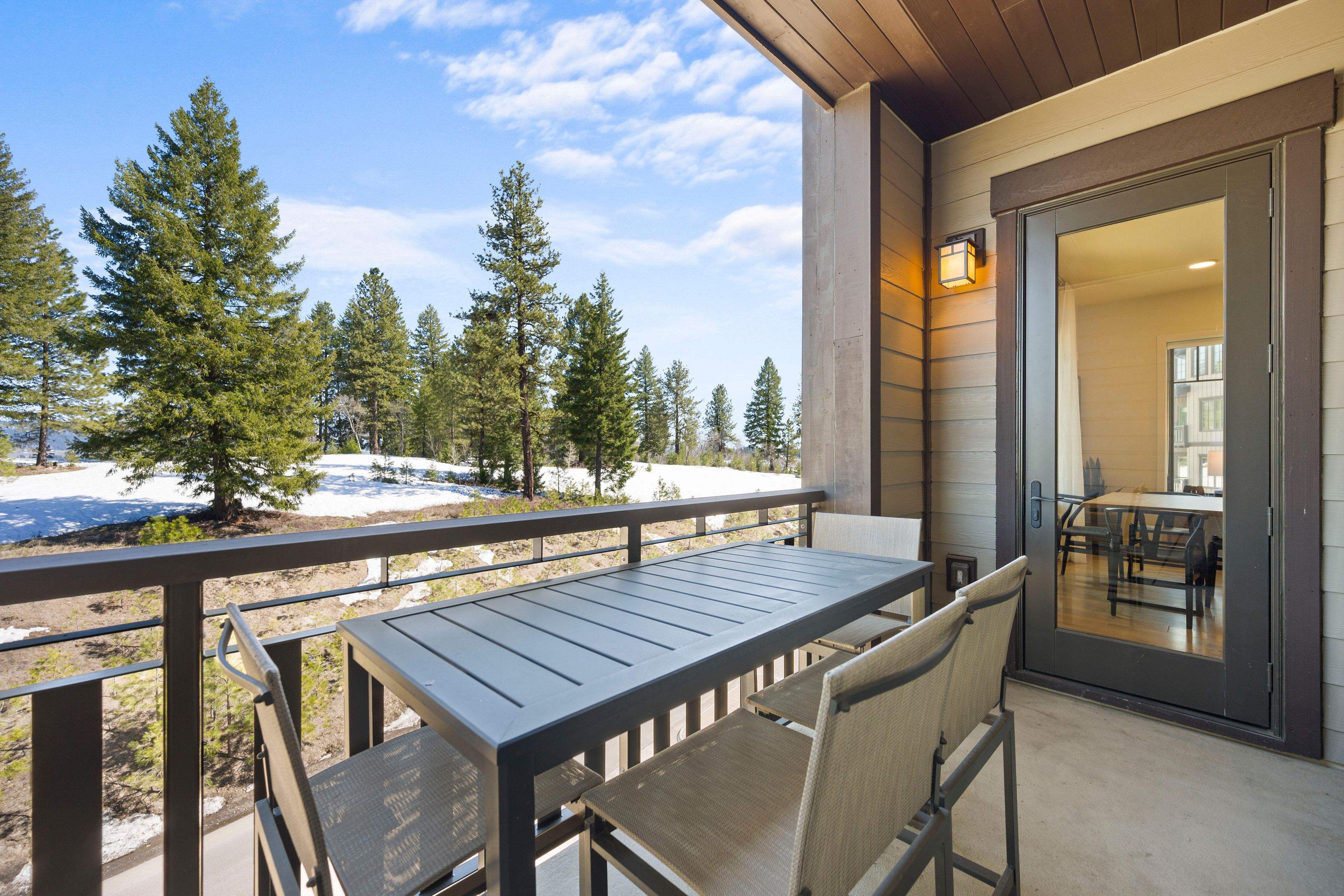 A balcony with a table and chairs, overlooking a snowy landscape with trees.