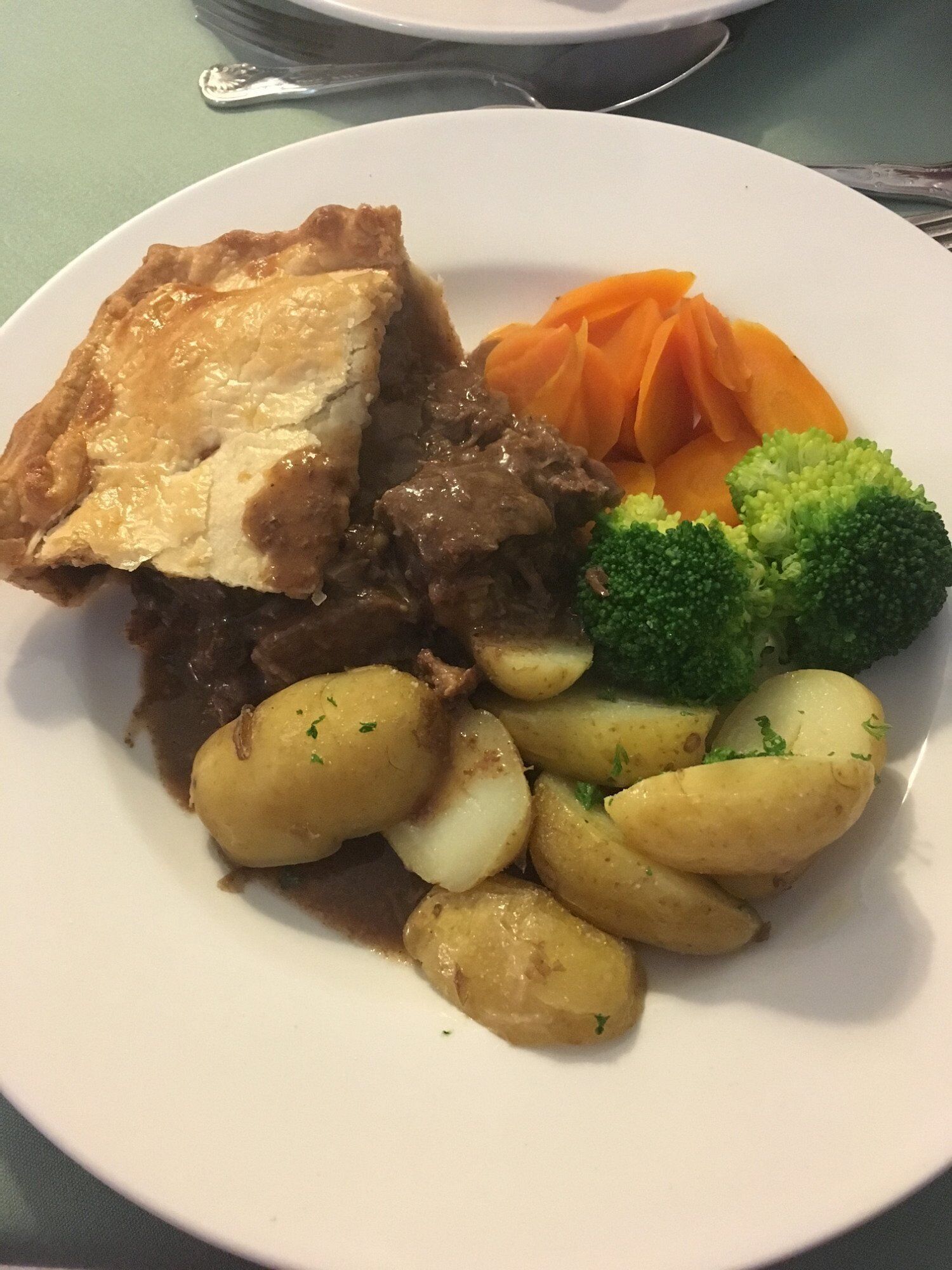 Un plato con una porción de pastel, carne de res, zanahorias, brócoli y papas.