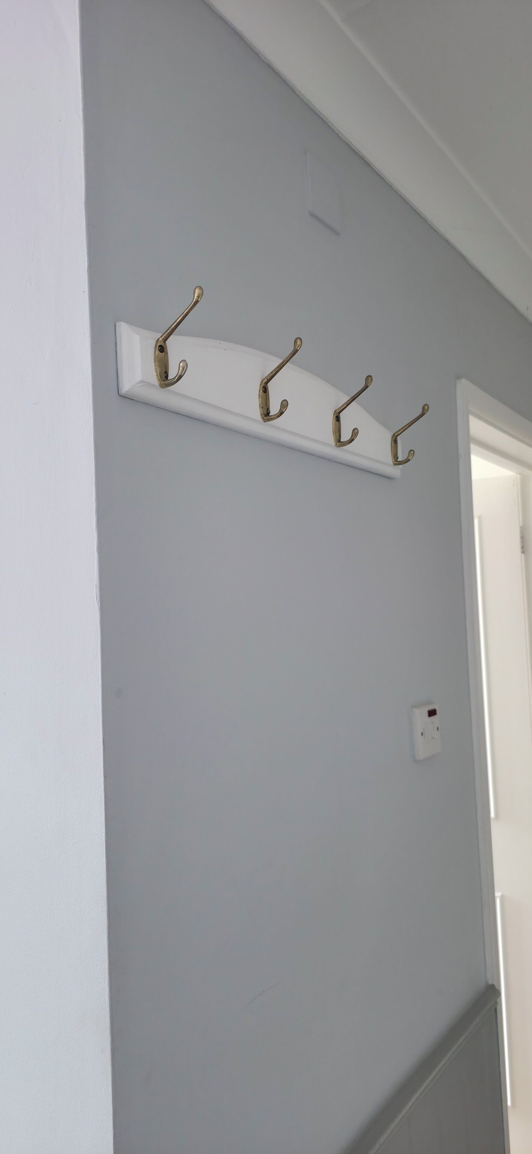 A white wall with a white shelf holding four gold-colored hooks.