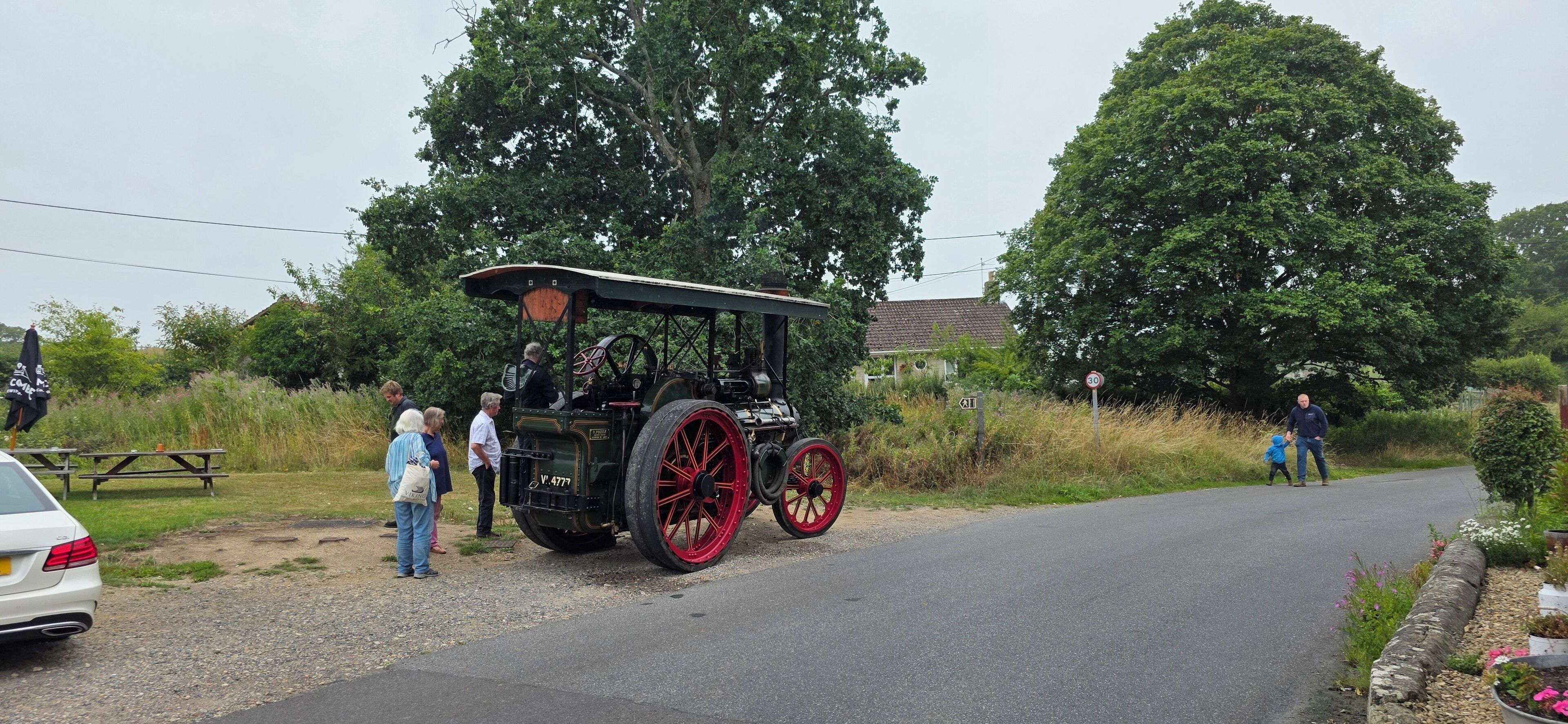 A vintage car parked on a rural road with people standing nearby.