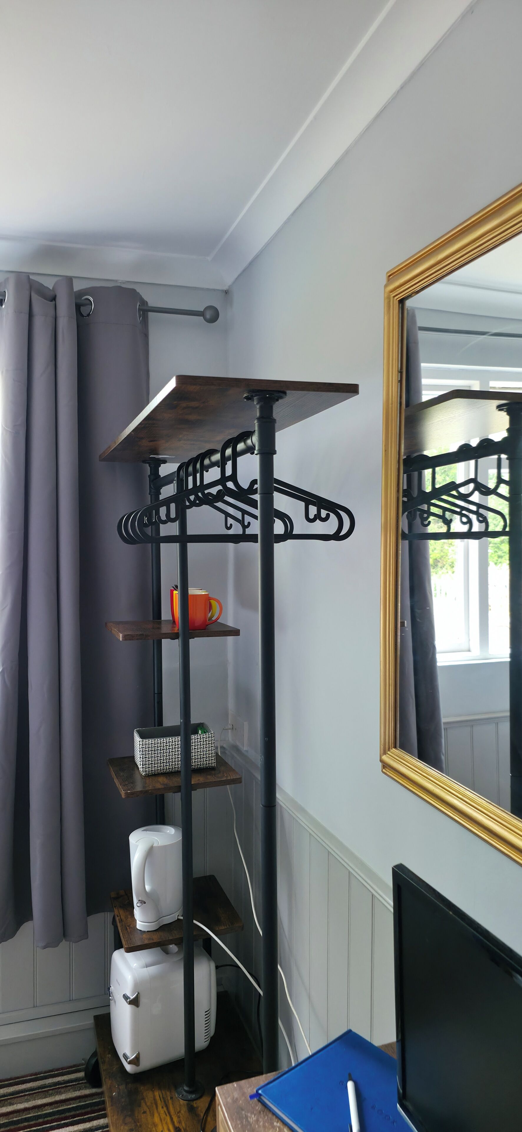 Una habitación de esquina con un estante metálico negro, un espejo y un electrodoméstico blanco.
