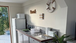 Eine moderne Küche mit einem weißen Kühlschrank, einer Mikrowelle und einem Spülbecken. Holzschränke und ein Pflanzentopf auf der Arbeitsplatte.
