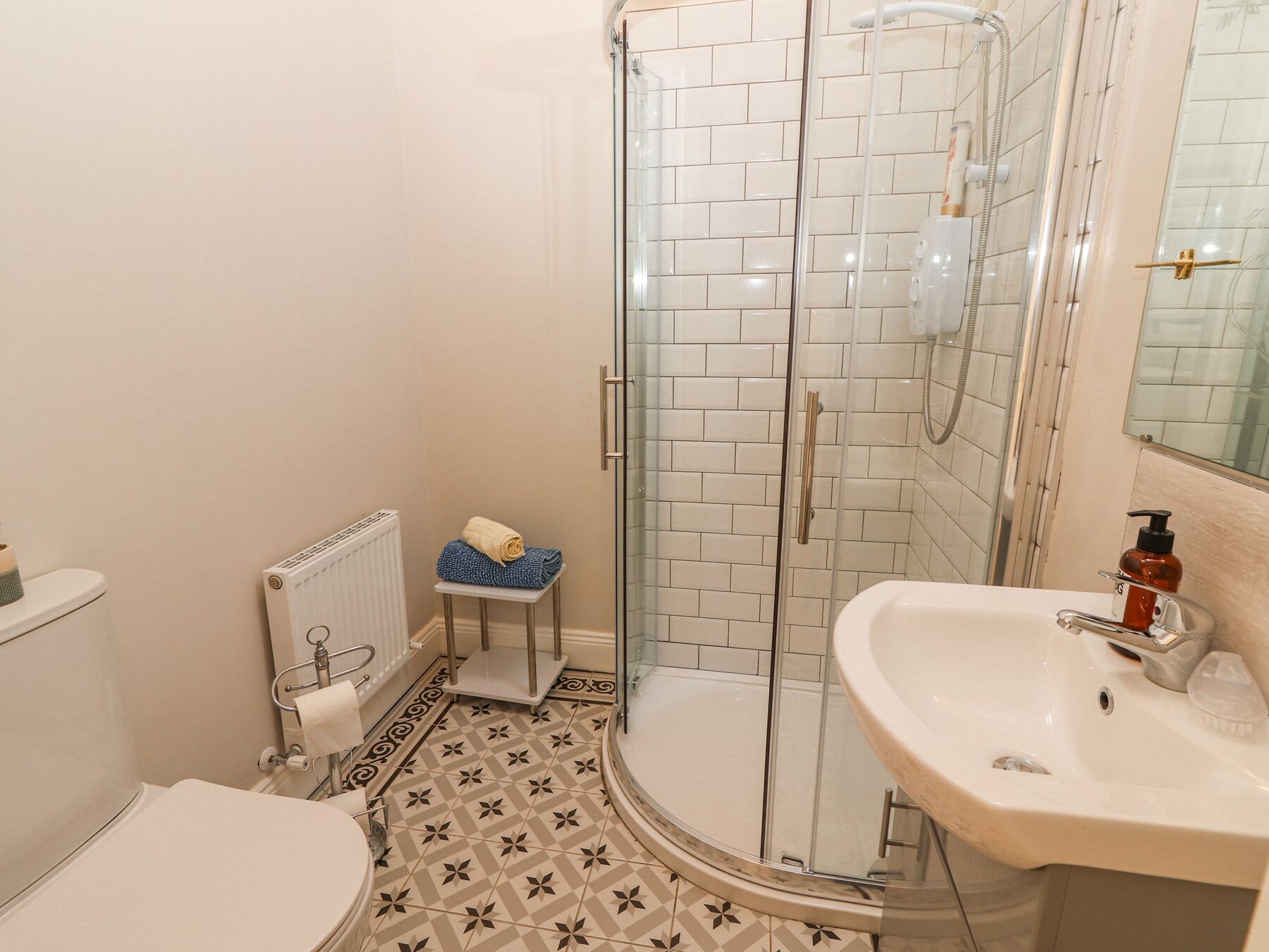 Un baño con ducha de vidrio, un lavabo blanco con dispensador de jabón y un inodoro.