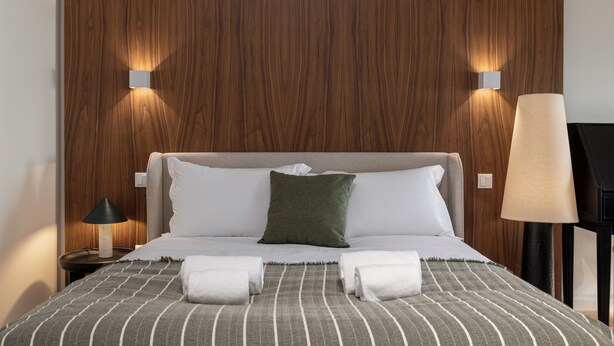 A neatly made bed with a striped blanket, two pillows, and two rolled towels. - Albertina Carlos Alberto By Aspasios (Porto)