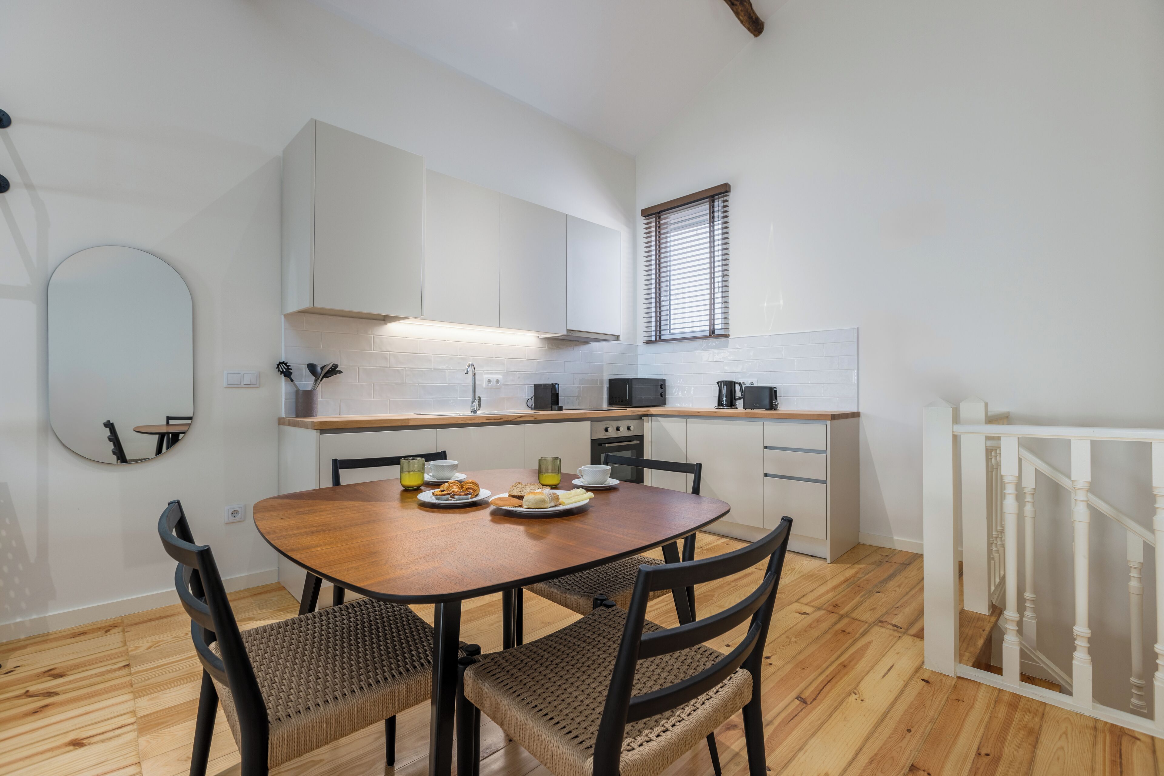 A modern kitchen with white cabinets, a wooden dining table, and a breakfast setting.