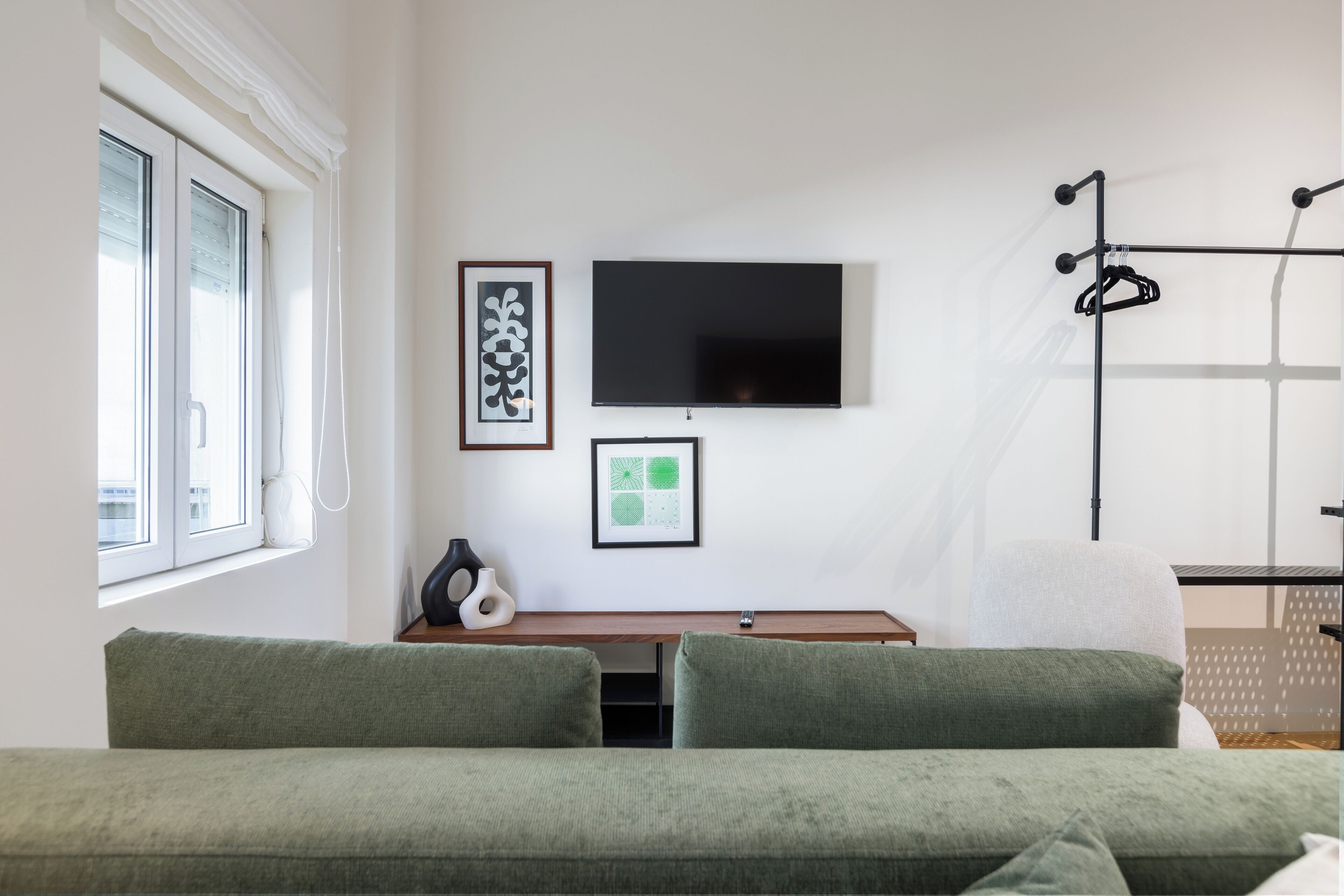 Et moderne værelse med en grøn sofa, et fladskærms-TV og et knagered.