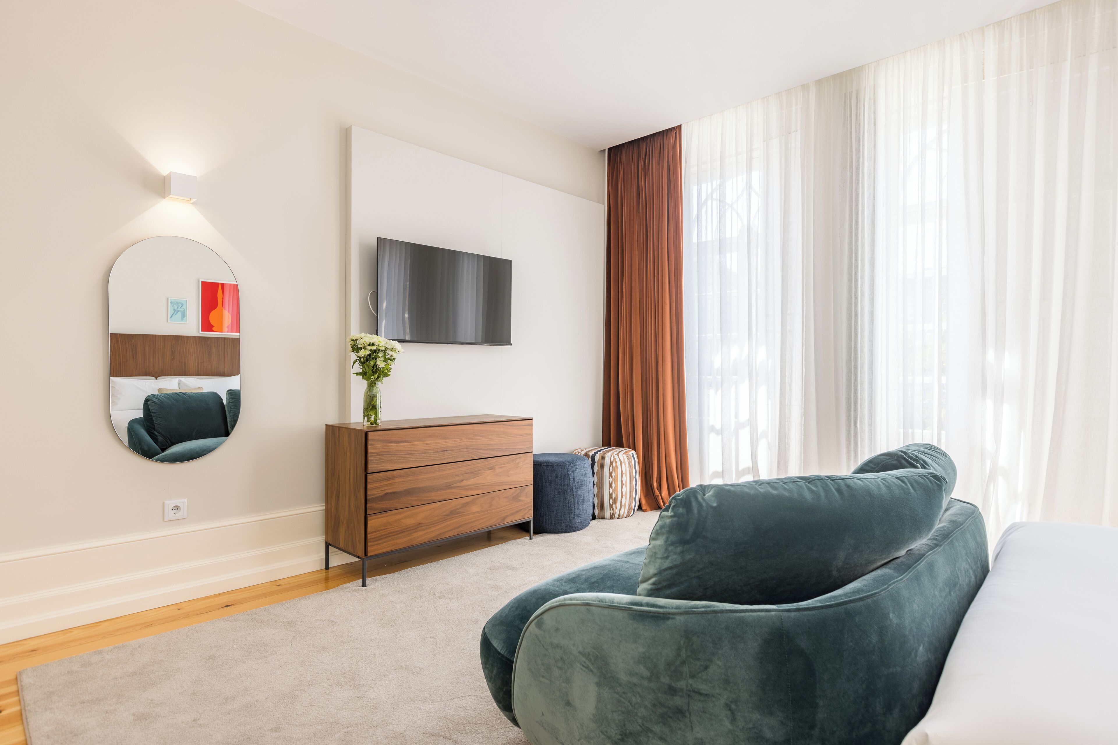Una camera da letto moderna con un letto grande, una TV a parete, un comò in legno e un'ampia finestra con tende.