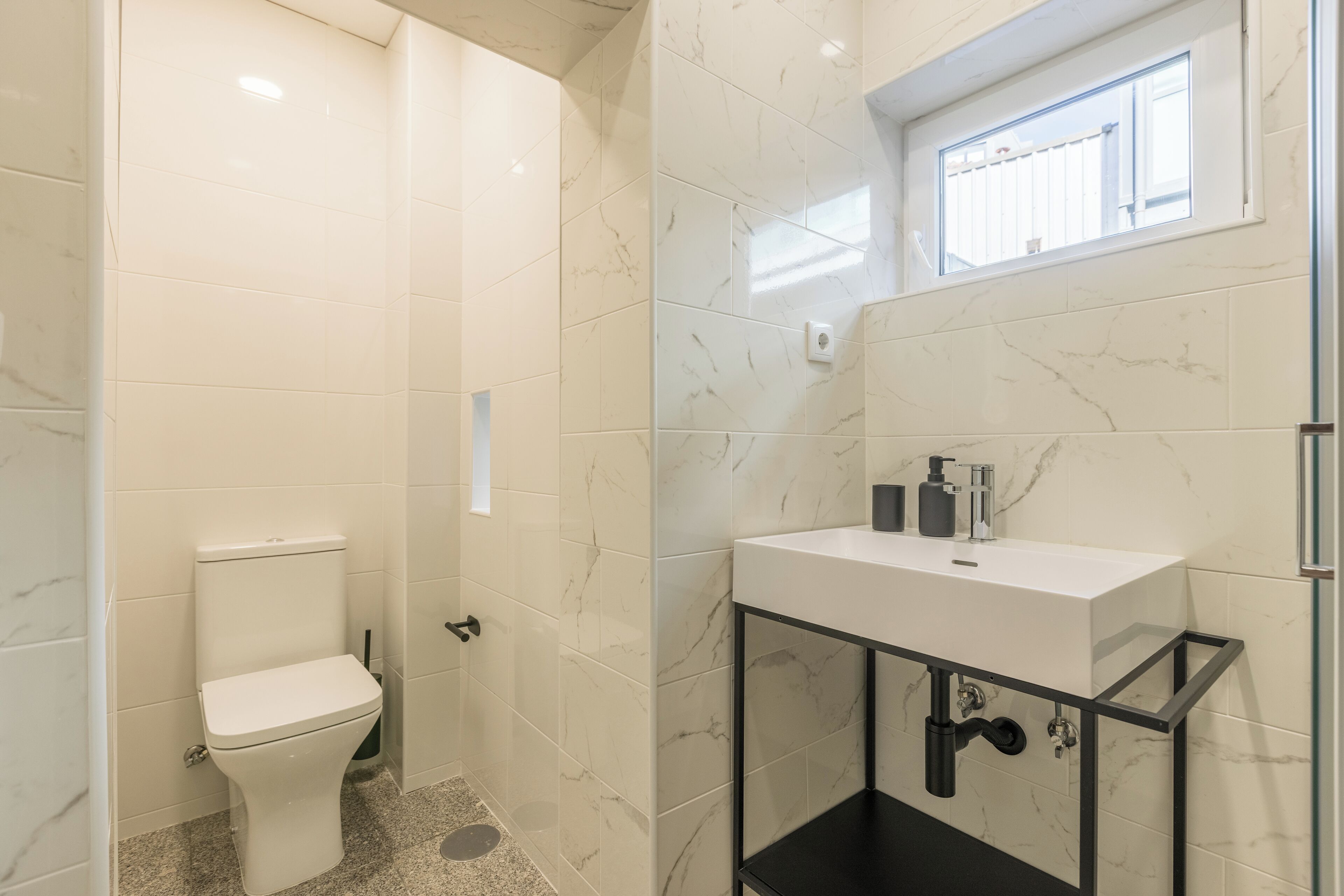 A modern bathroom with a toilet, a sink with a black frame, and a window above the sink.