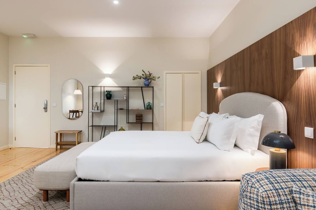 Un dormitorio moderno con una cama grande, una mesita de noche, un armario, un espejo y una pequeña mesa.