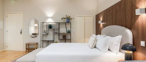 A modern bedroom with a large bed, a bedside table, a nightstand, a wardrobe, a mirror, and a small table.