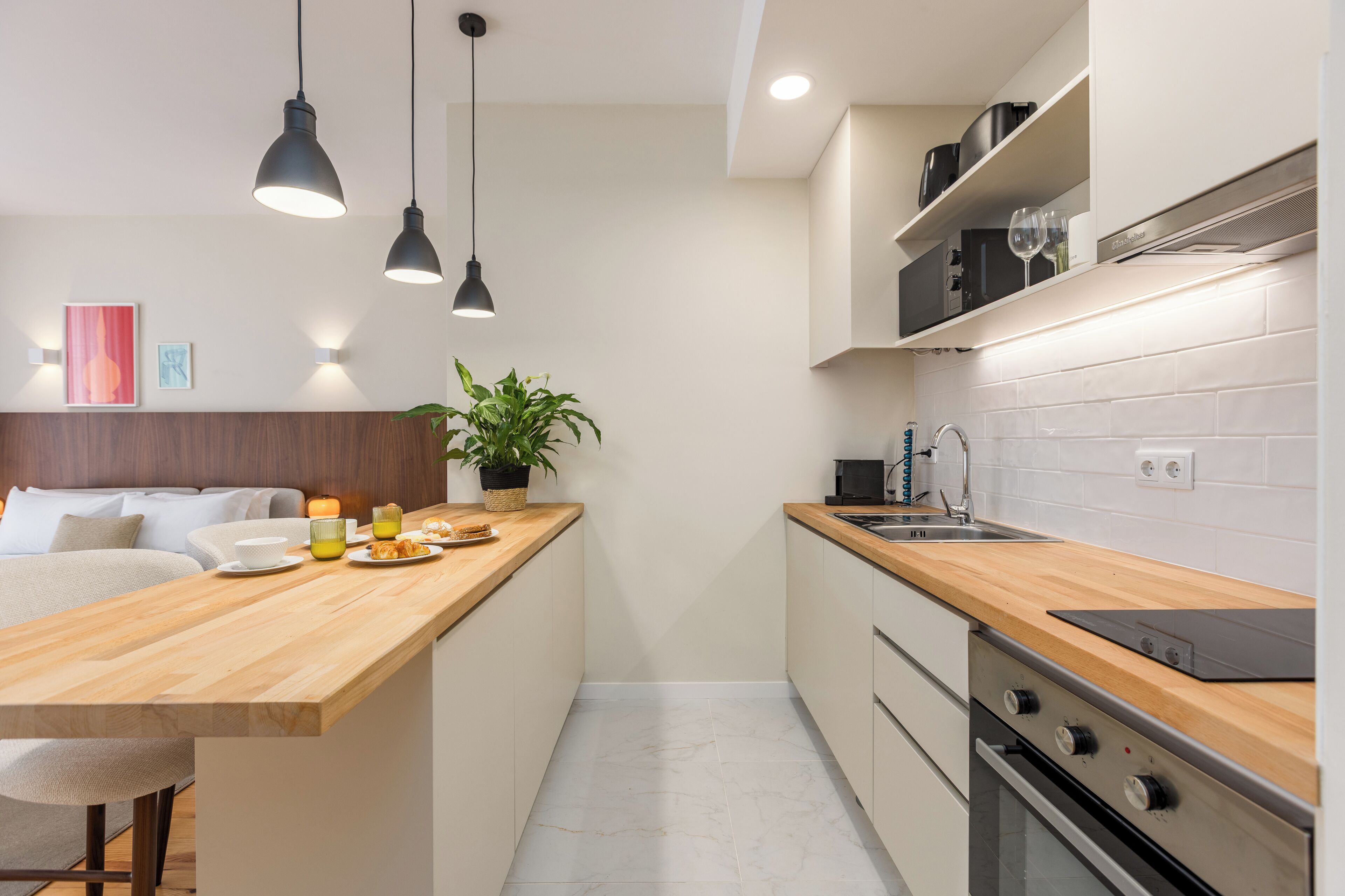 A modern kitchen with a wooden island, pendant lights, a potted plant, and a built-in oven.