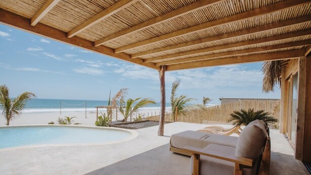 Un espace extérieur abrité comprenant une piscine, des chaises longues et une vue sur la plage.