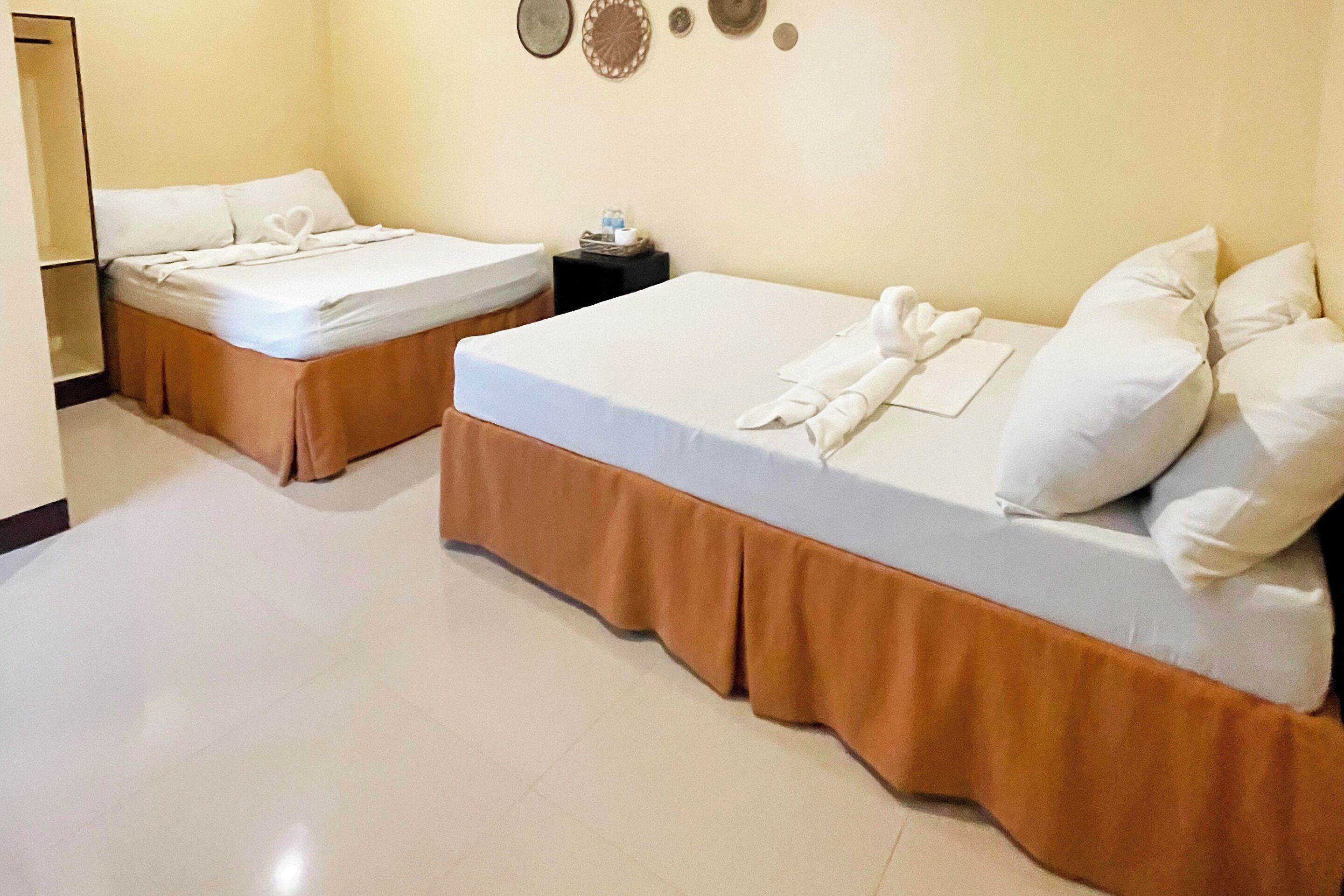 Two single beds with white linens and brown bed skirts in a hotel room.