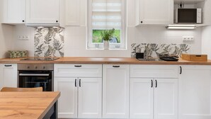 A modern kitchen with white cabinetry, a wooden countertop, and a window with blinds. - Nice apartment for 4 guests with WIFI, TV, patio and pets allowed (Nový Bor)