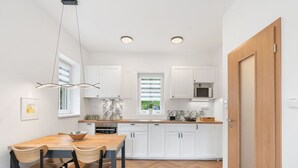 A modern kitchen with white cabinets, a wooden dining table, and a herringbone floor pattern. - Nice apartment for 4 guests with WIFI, TV, patio and pets allowed (Nový Bor)