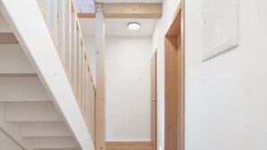 Un pasillo estrecho con una escalera de madera a la izquierda y una puerta de madera a la derecha.