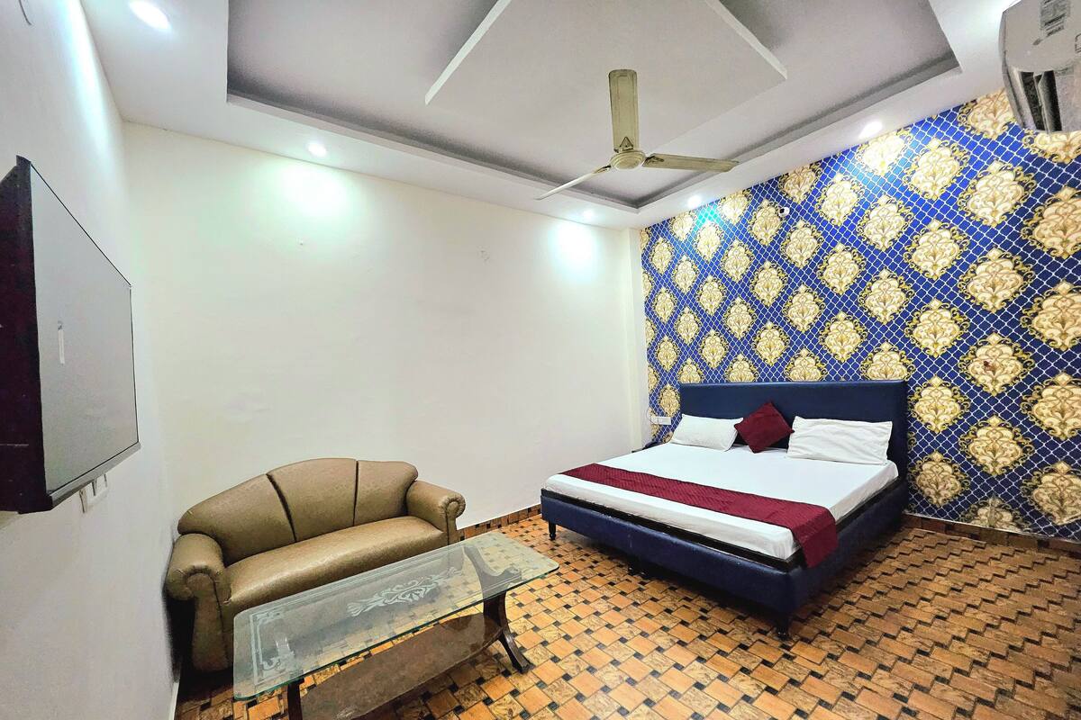 Un dormitorio con cama, una silla, una mesa, ventilador de techo y paredes con diseño.