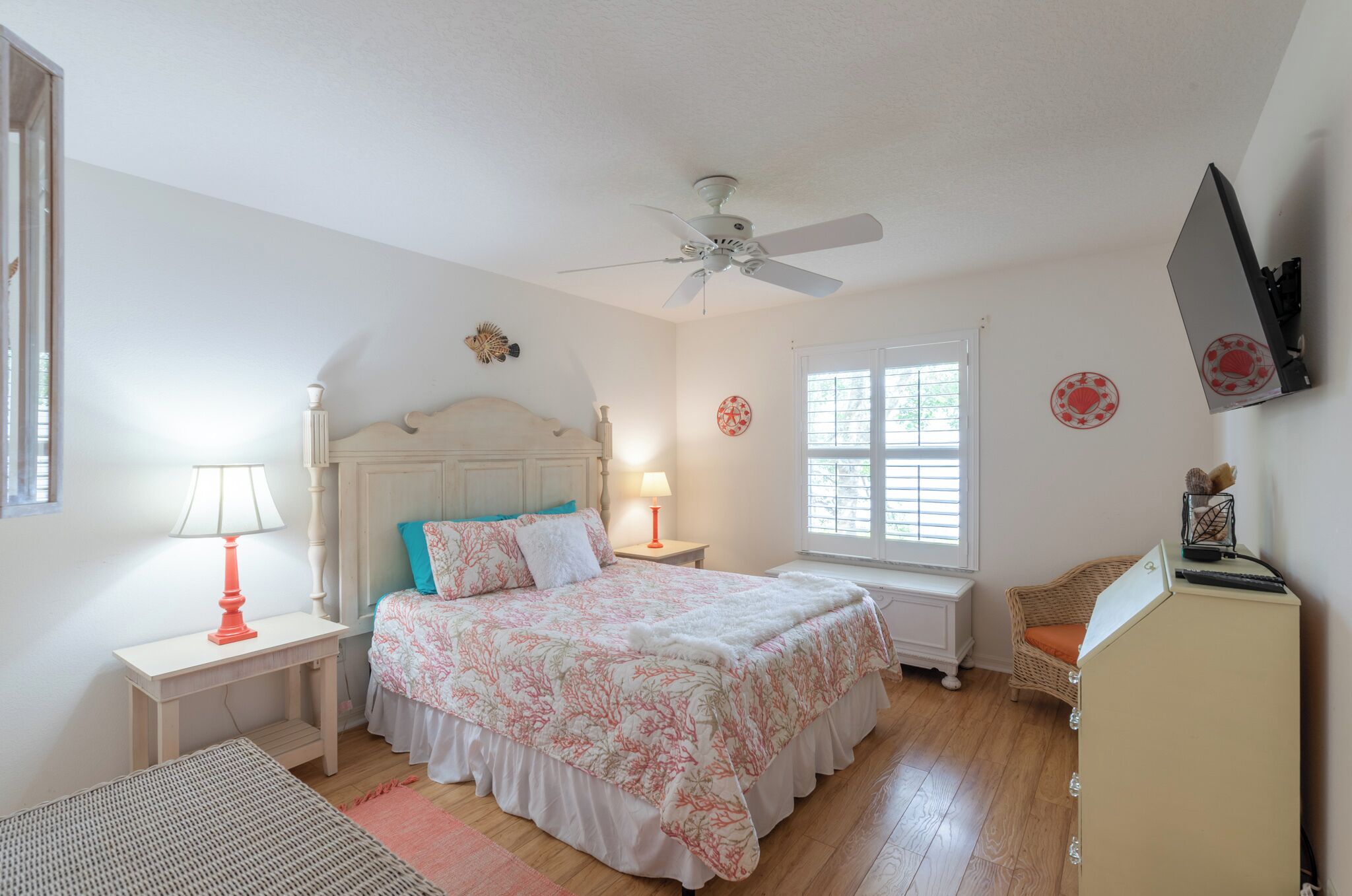Quarto com cama, ventoinha no teto, janela, mesa de cabeceira, abajur e cômoda.
