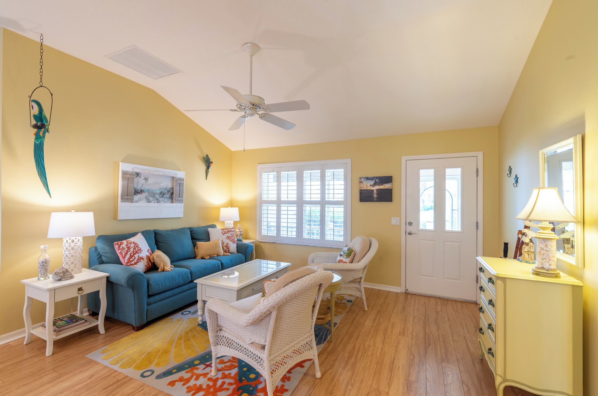 A living room with a blue sofa, white armchairs, a coffee table, and a ceiling fan.