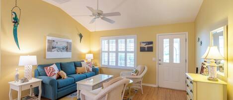 A living room with a blue sofa, white armchairs, a coffee table, and a ceiling fan.