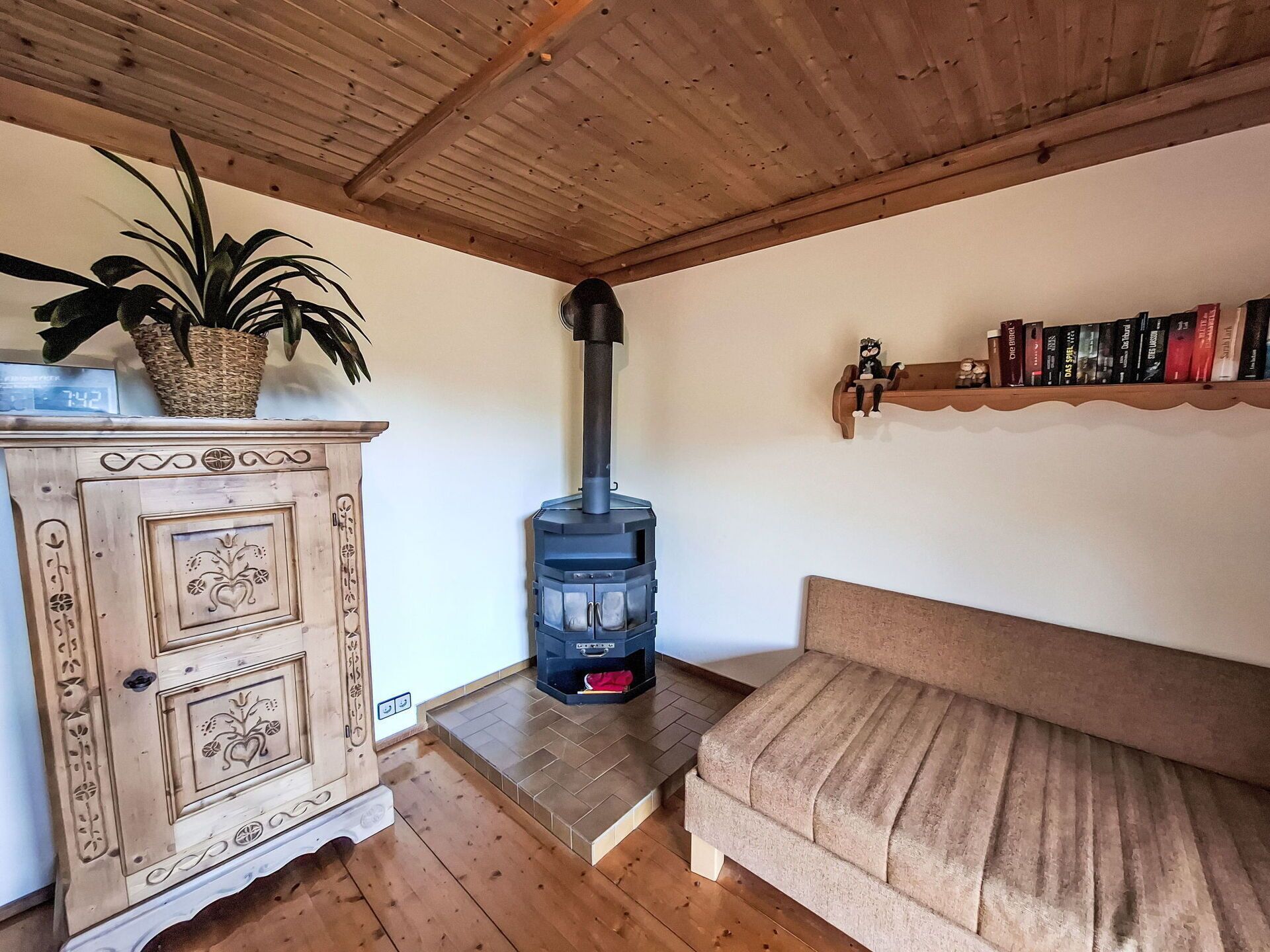 A cozy living room with a wooden ceiling, a decorative cabinet, a sofa, a bookshelf, and a large black heater.