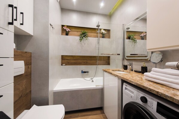 Une salle de bain moderne avec une baignoire blanche, un lave-linge encastré et des étagères en bois ornées de plantes.