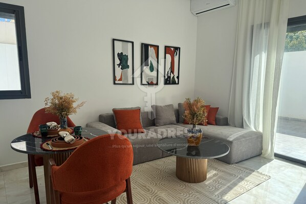A modern living room with a grey sofa, orange chairs, a glass coffee table, and abstract wall art. - Youradress (Casablanca)