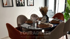 A dining area with a round table, chairs, and artwork on the wall. - Youradress (Casablanca)