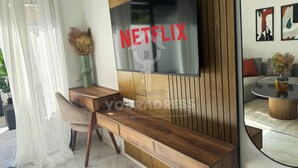 A modern living room with a wooden TV stand, a glass coffee table, and a sofa with a red cushion. - Youradress (Casablanca)