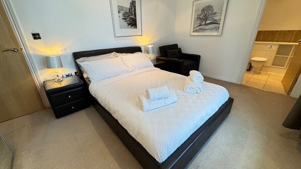 A neatly made bed with white linens and towels, a bedside table with a lamp, and a nightstand. - Oval House Retreat in Camden Town (London)