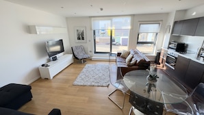 A modern living room with a flat-screen TV, a zebra-patterned chair, a brown leather sofa, a glass dining table, and a kitchen with a microwave and oven. - Oval House Retreat in Camden Town (London)