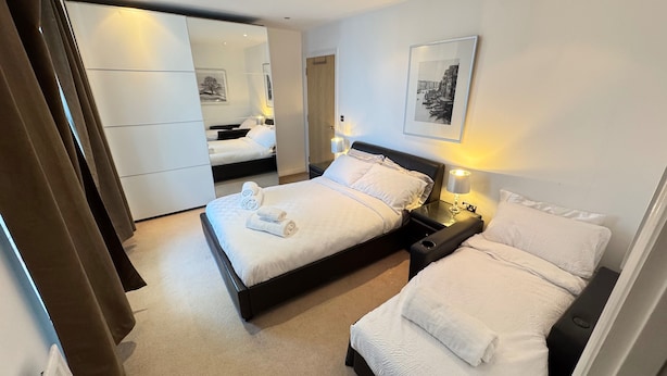 A hotel room with a large bed, a smaller bed, a nightstand with a lamp, a wardrobe, and a mirror. - Oval House Retreat in Camden Town (London)
