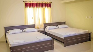 A hotel room with two single beds, a nightstand, a window with curtains, and a light switch on the wall.