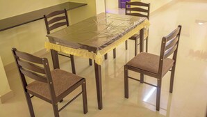 A dining area with a table covered by a protective sheet, four wooden chairs with cushioned seats, and a yellow lace tablecloth.